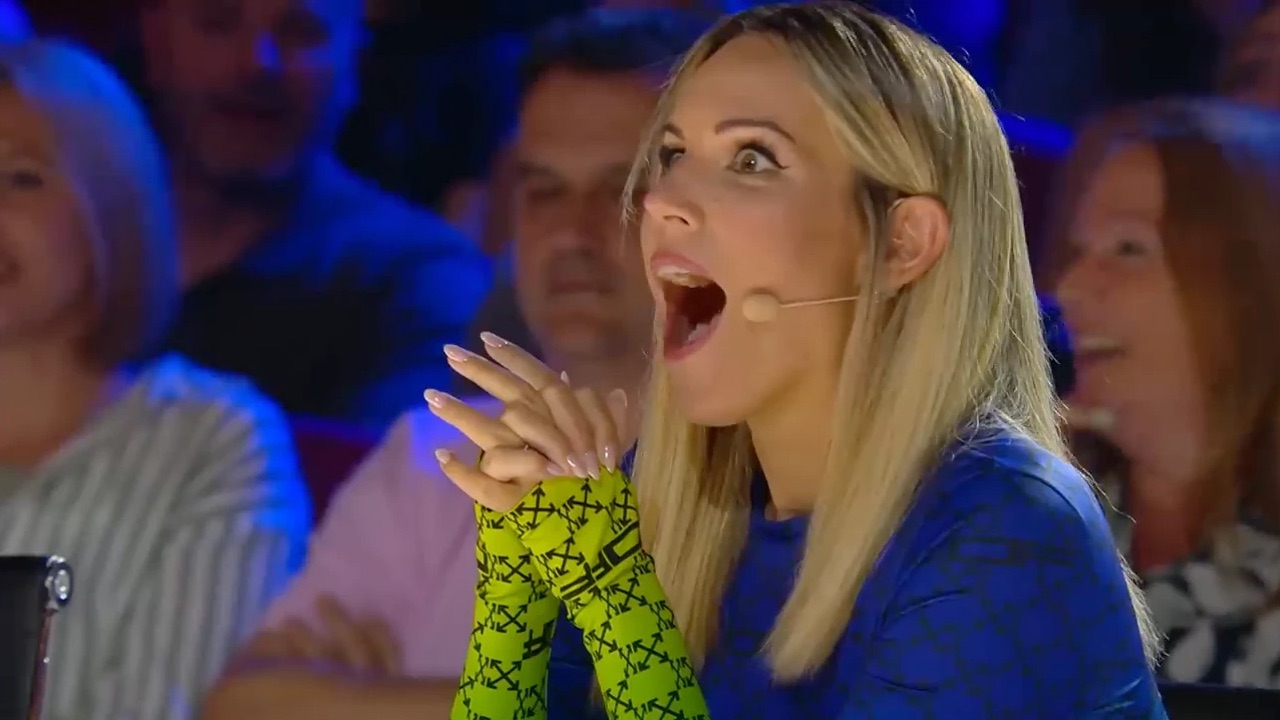 Una giudice di un talent show televisivo a bocca aperta, con le mani giunte, durante un numero di Sergio Starman
